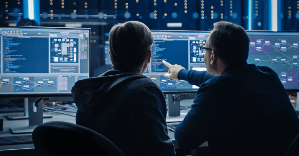 Two colleagues reviewing cybersecurity threat data on computer monitor 
