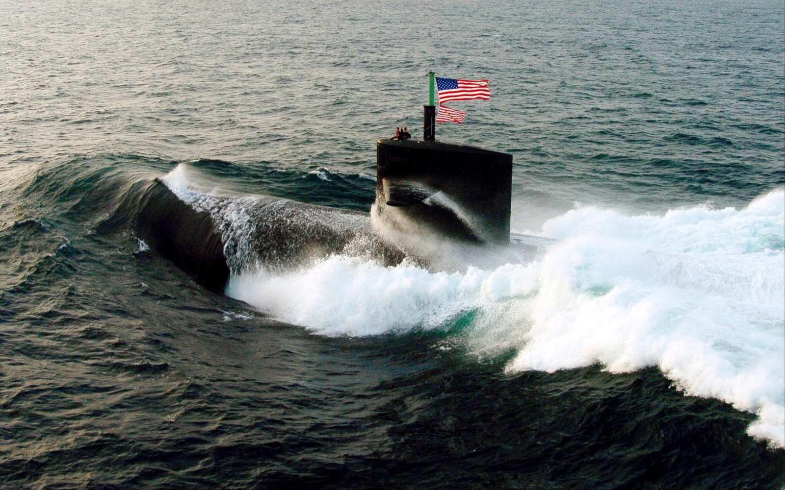 A US Navy submarine surfacing under way, national ensign flying