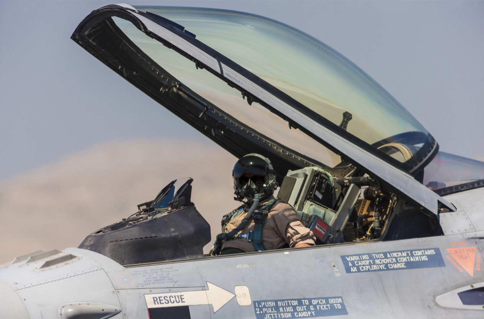 A fighter pilot at the controls, canopy raised.
